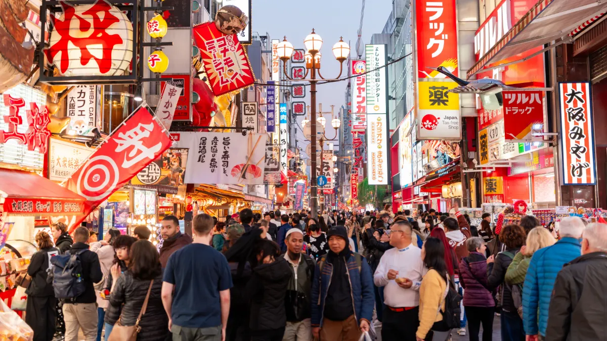 Crowded Osaka shopping street lined with colorful Japanese signs, lanterns, restaurants and pedestrians.