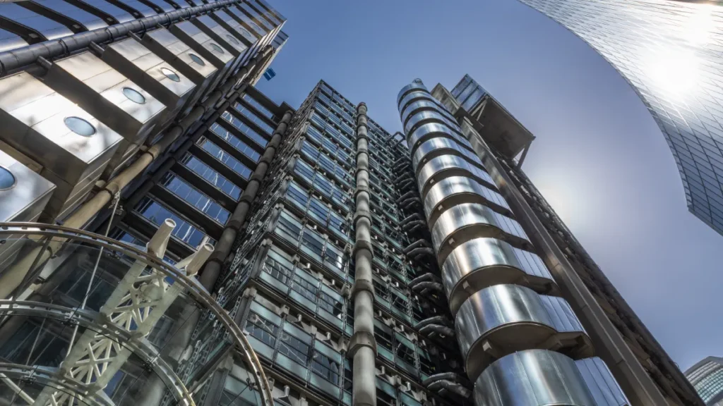 Upward view of modern office towers with exposed pipes, metal cladding and curved glass structures.