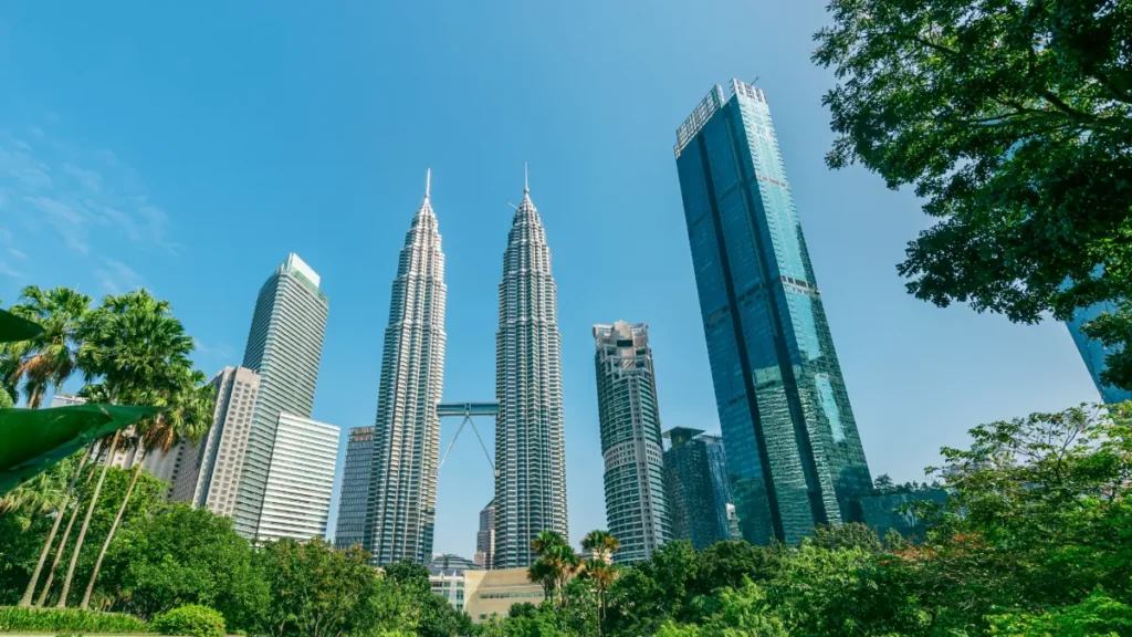 Kuala Lumpur skyline featuring the Petronas Twin Towers and surrounding skyscrapers above lush greenery.