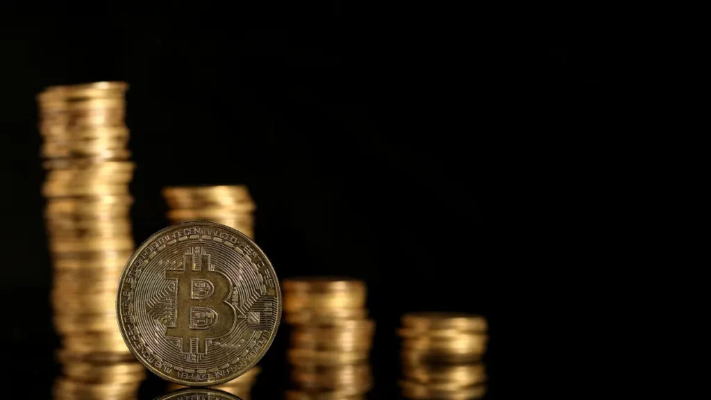 Stacks of gold coins surround a Bitcoin coin against a black background.