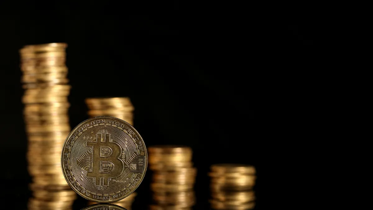 Stacks of gold coins surround a Bitcoin coin against a black background.