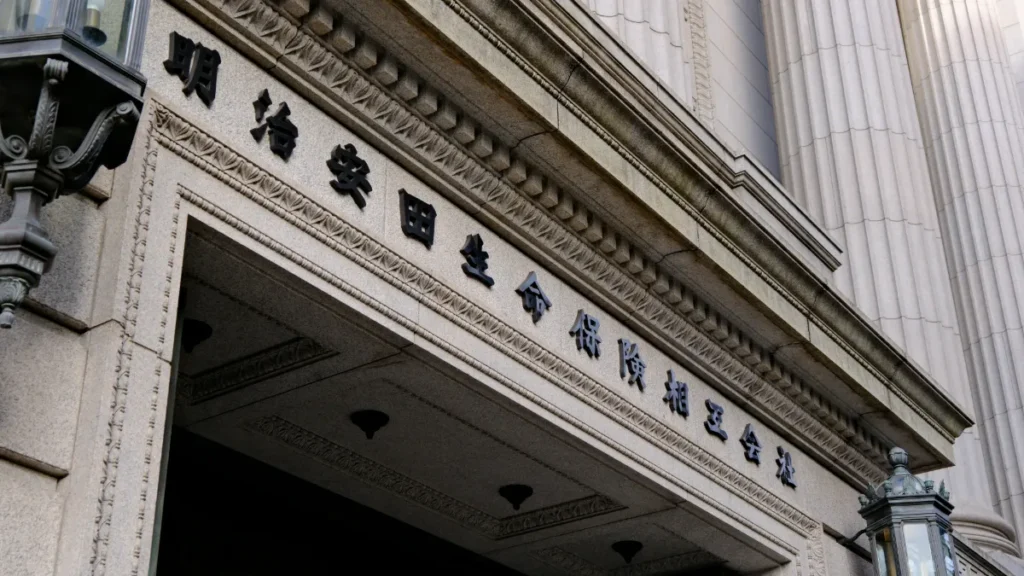Meiji Yasuda Life Insurance Company building entrance with Japanese lettering on its stone façade.