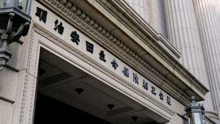 Meiji Yasuda Life Insurance Company building entrance with Japanese lettering on its stone façade.