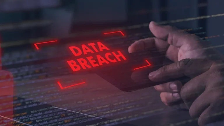 Hands hover over a tablet displaying red “DATA BREACH” text above lines of computer code.