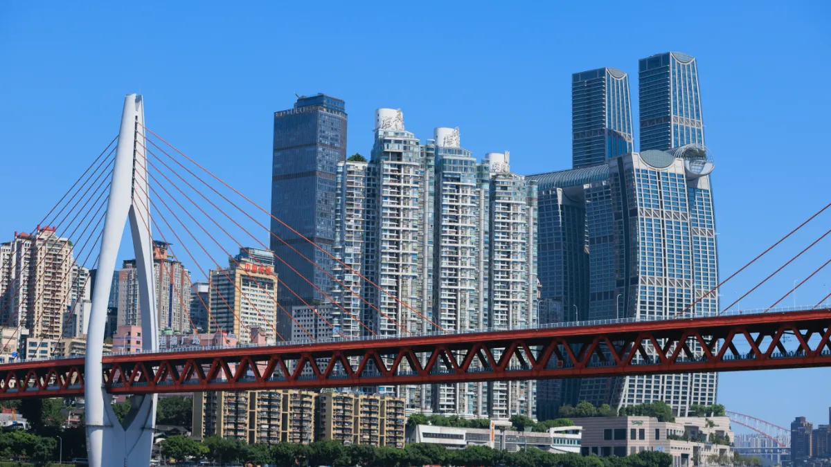 A cable-stayed bridge spans a dense city skyline of high-rise buildings beneath a clear blue sky.