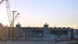 Data center construction site with cranes, fencing and industrial buildings at sunset.
