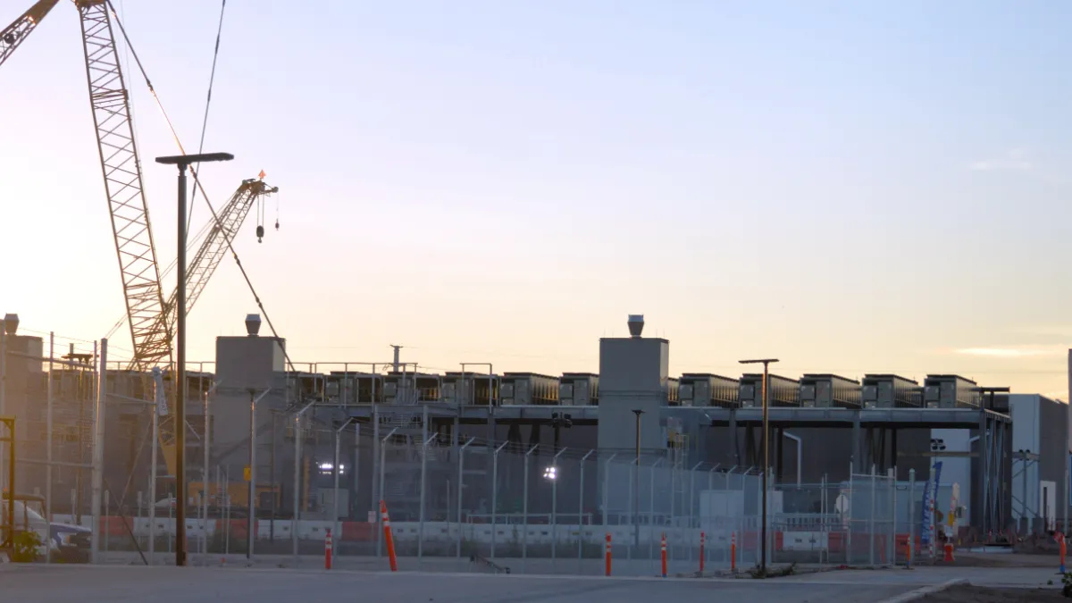 Data center construction site with cranes, fencing and industrial buildings at sunset.
