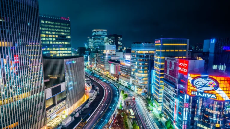 Nighttime Tokyo cityscape with illuminated Japanese signs, high-rises and curving multilane traffic.
