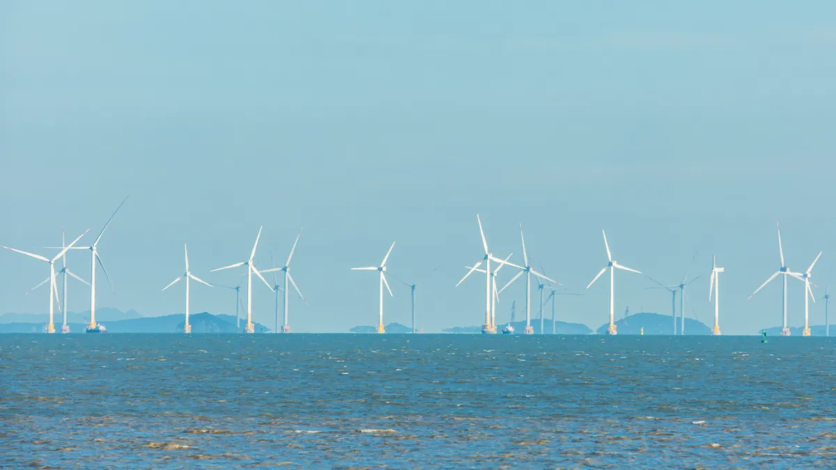 Offshore wind turbines stand in rows across the sea under a blue sky.