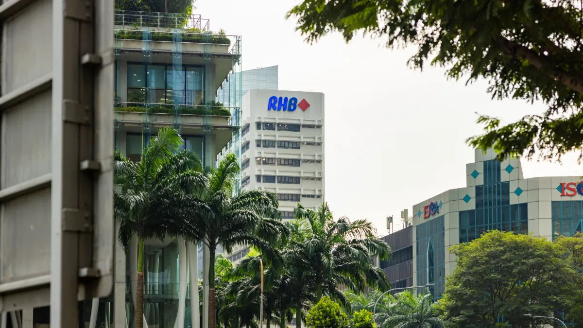 Urban office buildings displaying RHB and other company logos, framed by palm trees.