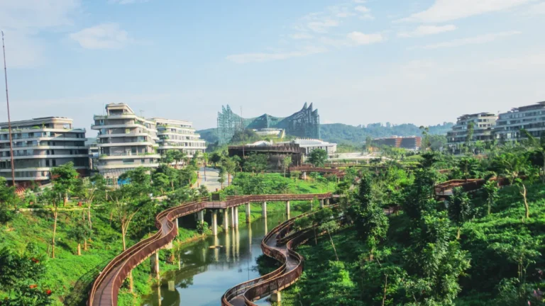 Modern buildings surround a lush park with winding wooden walkways over a narrow waterway.