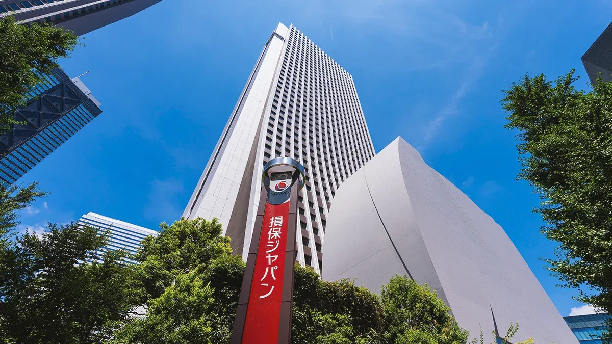 Sompo Japan office tower and sign viewed from below against a bright blue sky.