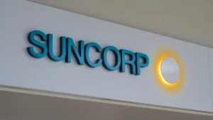 Suncorp cuts FY2027 GWP outlook on A$125m commercial contract loss, NZ dollar weakness Suncorp logo mounted on a white wall.