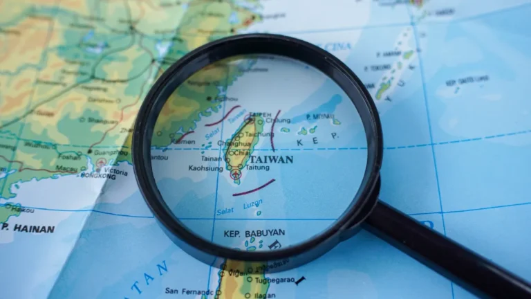 A magnifying glass highlights Taiwan on a map of East and Southeast Asia.