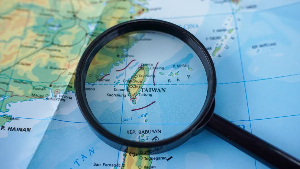 A magnifying glass highlights Taiwan on a map of East and Southeast Asia.