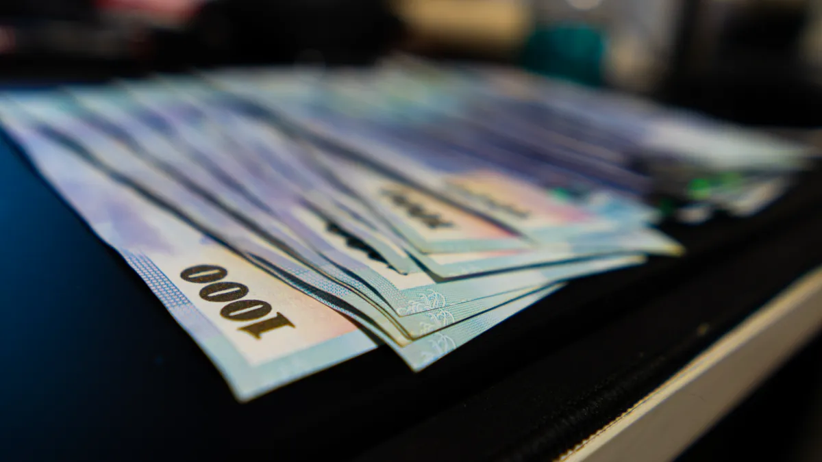 A fan of 1,000-dollar banknotes rests on a dark surface.