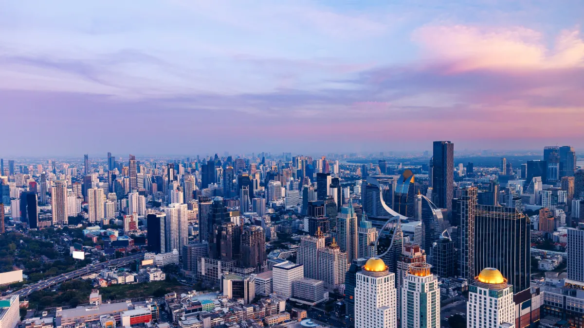 A dense city skyline stretches beneath a pink and blue sunset, with high-rise towers in the foreground.