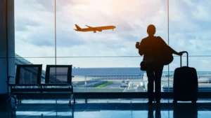 Traveler with luggage watches an airplane from an airport terminal window.