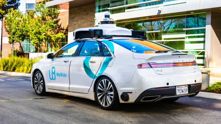 A WeRide autonomous car with roof-mounted sensors parked outside a modern building.